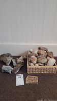 Wicker basket full of various decorative rocks and two piles of rough rocks positioned next to it on a carpeted floor.