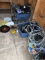 Two blue totes filled with various outdoor solar lights, metal lawn ornaments, tubing, and garden items placed on a shed floor.