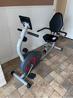 Side view of the full stationary recumbent bike showing seat, pedals, and display.