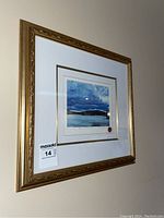 Framed print hanging on wall with gold decorative frame and white mat with gold accent