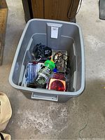 Plastic tote bin open showing assorted packaged items including magnetic tow lights, battery controller, bungee cord, and other accessories.