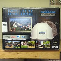 Front view of the box showing Winegard Carryout portable satellite TV antenna with compatibility logos of Dish, DirecTV, and Bell; promotional images of usage at campsites and RVs; Realtree AP camo option noted.