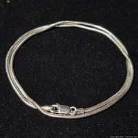 Full view of coiled sterling silver chain necklace on black background showing overall shape and clasp closed.