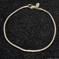 Front view of a sterling silver snake chain bracelet laid flat on black background, showing the full length and clasp.