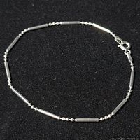 Front view of the silver bracelet formed in a loose circle, showing the alternating bead and tube link pattern and lobster clasp.