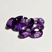 Clear view of seven faceted amethyst gemstones arranged together on a white background showing their color and cut.
