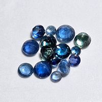 Collection of loose faceted blue sapphire gemstones in assorted sizes and shades of blue on white background.