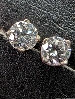 Close-up photo of two round-cut lab grown diamond stud earrings set in 14k white gold prong settings on a textured black surface.