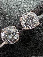 Close-up of pair of earrings on black background showing round brilliant diamonds in four-claw 14k white gold settings