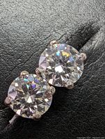 Pair of round moissanite stud earrings in four-prong 14k white gold settings on a black textured background