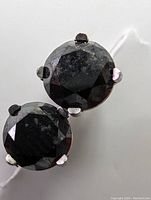 Close-up photo of earrings showing round faceted black diamonds in 4-prong 14k white gold setting.