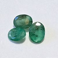 Three oval faceted emerald gemstones shown on a white background, highlighting color and inclusions.