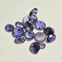 Faceted loose iolite gemstones in various shades of purple and violet-blue, displayed on a light background.