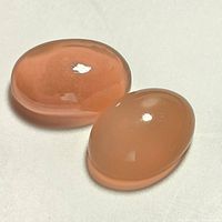Two polished oval cabochon moonstones on white background, showing peach color and smooth domed surface.