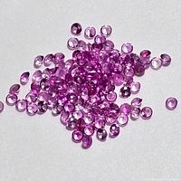 Close-up image showing a pile of small round faceted pink sapphire gemstones on a white background, highlighting their color and cut.