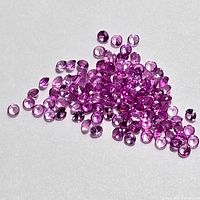 Close-up photo of numerous small natural pink sapphire gemstones laid on a neutral background, showing their round faceted cuts and pink hues.