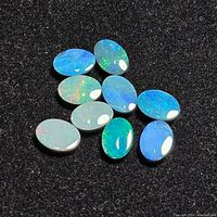 Ten oval polished opal cabochons on black background showing play of blue and green colors