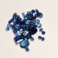 Photo showing multiple loose blue sapphires in various cuts and sizes arranged on a white surface.