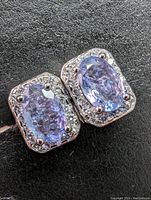 Close-up photo of sterling silver earrings with oval natural tanzanite gemstones and clear stones halo.