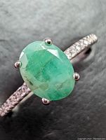 Close-up of oval green emerald gemstone on sterling silver ring, showing natural inclusions and prong setting.