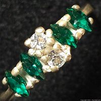 Close-up image showing the sterling silver ring with alternating green marquise-cut stones and two clear round stones on black background.