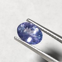 Close-up image of oval cut tanzanite held by tweezers showing faceted surface and color.