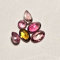 Loose assorted tourmaline gemstones in mixed shapes and colors on plain background showing size and color variations