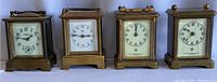 Front view showing four vintage brass travel clocks side by side, varying handle and face designs.