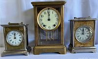 Front view of three brass mantel clocks showing varying sizes and dial styles