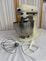 Front view of Kitchenaid Chef Model K45Ss stand mixer in cream with stainless steel bowl and two attachments laid in front.