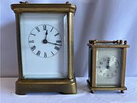 Front view of both brass mini window clocks side by side showing dial and size difference.