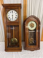 Full view of two wooden ornate wall clocks side by side, showing their overall design and size difference.