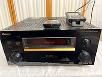 Front view of Pioneer VSX-59TXi multi-channel receiver with included remote control on top. Display panel lit, showing powered-on status.