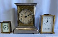 Front view of three clocks: center clock with brass engraved panel and two smaller rectangular brass clocks on sides
