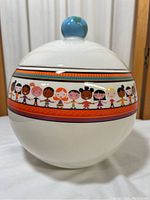 Front view of white ceramic UNICEF cookie jar with colorful children band and globe knob on lid