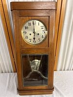 Full view of vintage Gustav Becker wall clock showing oak wood case with glass pendulum window and silver clock face with black numbers and hands.