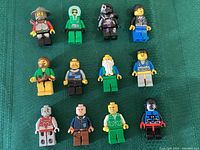 Top-down view showing all 12 LEGO mini figures arranged in rows on a green surface, highlighting the variety of characters and colors.