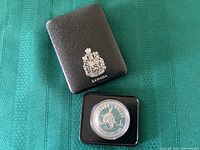 Black faux leather case with Canadian coat of arms embossed on top and the silver coin specimen housed in a black plastic frame inside.
