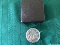 Closed black display case for the coin shown with the coin outside.