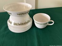 Stack of six white Corelle cereal/soup bowls with green floral band around the rim beside one matching coffee/tea cup.