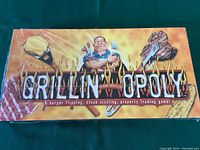 Front view of sealed Grillin'-opoly board game box with flame-themed design and cartoon character grilling