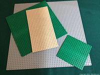 Four LEGO base plates of varying sizes and colors arranged overlapping on a flat surface, showing scales from small to large.