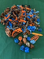 Wide assortment of LEGO Bionicle parts laid out showing various masks, limb pieces, and joint components in multiple colors like blue, brown, orange.