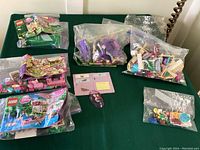 Image displaying assorted Lego Disney Princess parts and figures in multiple plastic bags along with instruction manuals placed on a green surface.