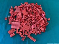 Pile of assorted red LEGO bricks of various shapes and sizes on a teal fabric surface.