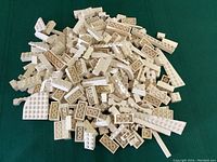 Overview photo showing a pile of assorted white Lego bricks and pieces of varied shapes and sizes on a green background.