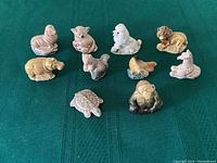 Top view showing all 10 Red Rose Tea figurines arranged on green fabric: a lion, poodle, pig, squirrel, hen, leopard, hippo, cat, monkey, and turtle