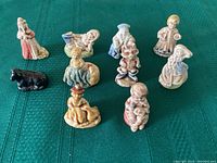Top view of 10 Red Rose Tea nursery rhyme ceramic figurines laid out on green textile