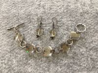 Photo of silver bracelet with large crystal beads and earrings arranged on grey fabric background.