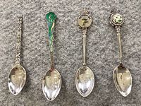 Four Canadian sterling silver souvenir spoons lined up showing detailed handles and decorative enamel and motifs.